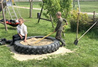 Kinder spielen in einem Sandkasten aus einem großen Reifen bei Safari Tent auf Boerencamping Swarthoeve, Niederlande.
