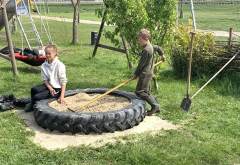 Kinder spielen in einem Sandkasten aus einem großen Reifen bei Safari Tent auf Boerencamping Swarthoeve, Niederlande.