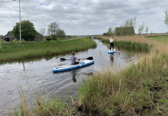 Two people paddle on a small waterway near Safari tent at Boerencamping Swarthoeve in the Netherlands.