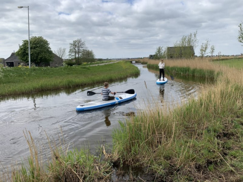 Two people paddle on a small waterway near Safari tent at Boerencamping Swarthoeve in the Netherlands.