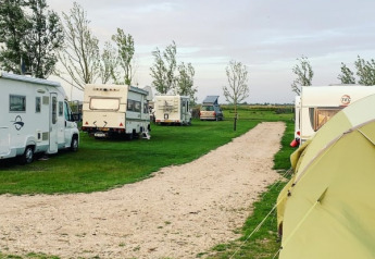 Wohnmobile und ein Safarizelt auf dem Bauern-Campingplatz Swarthoeve in den Niederlanden bei Sonnenuntergang.