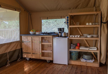 Kitchen area inside a safari tent at Vakantiepark de Toffe Peer, Netherlands, featuring wooden shelves and fridge.