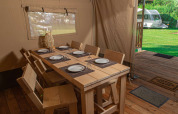 Comedor en tienda safari con mesa de madera para seis en Vakantiepark de Toffe Peer, Países Bajos.