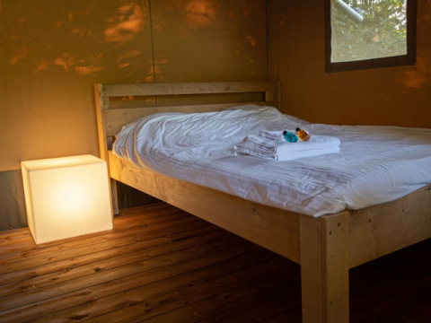 Interno di tenda safari a Vakantiepark de Toffe Peer, Paesi Bassi, con letto e lampada a cubo illuminata.