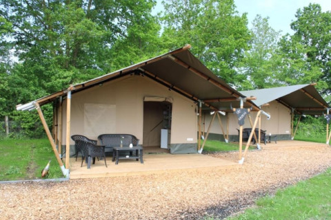 Zwei Safarizelte auf einem Campingplatz mit Veranda und Gartenmöbeln, umgeben von Bäumen.