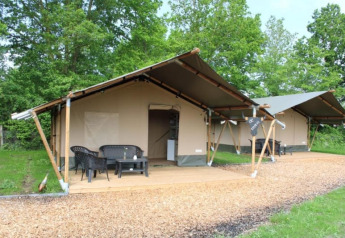 Tiendas safari en fila, con porches y sillas, ubicadas en un entorno de camping rodeado de árboles verdes.