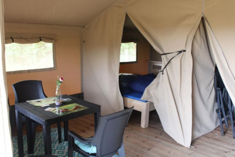 Interno di una tenda safari presso Camping de Waterbuffelfarm nei Paesi Bassi, con tavolo e letto.