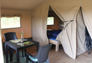 Interieur van een safaritent bij Camping de Waterbuffelfarm in Nederland met tafel, stoelen en bed.