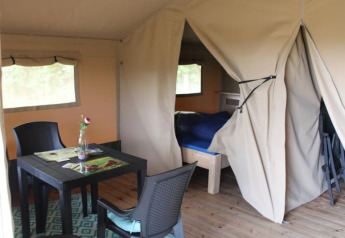 Intérieur d'une tente safari au Camping de Waterbuffelfarm aux Pays-Bas, avec une table et un lit visibles.