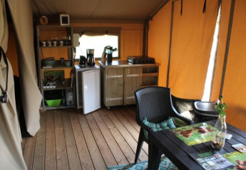 Innenansicht eines Safarizeltes mit Küchenzeile und Sitzbereich im Camping de Waterbuffelfarm, Niederlande.