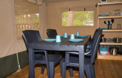 Interior de tienda safari con mesa negra, cuatro sillas y vajilla azul en Camping Aller-Leine-Tal, Alemania.