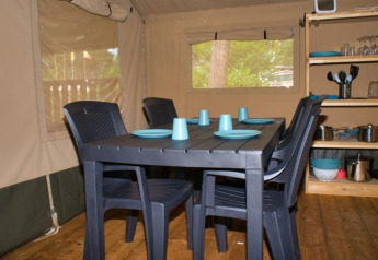 Interior de tienda safari con mesa negra, cuatro sillas y vajilla azul en Camping Aller-Leine-Tal, Alemania.