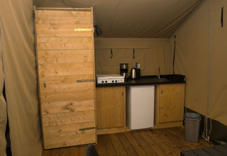 Interior de una tienda safari con pequeña cocina y puerta de madera en Camping Aller-Leine-Tal, Alemania.