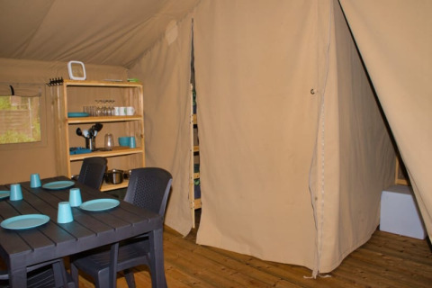 Innenansicht eines Safari-Zelts mit Esstisch, Stühlen und Regal auf dem Campingplatz Aller-Leine-Tal, Deutschland.