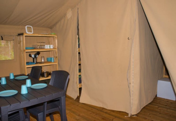 Innenansicht eines Safari-Zelts mit Esstisch, Stühlen und Regal auf dem Campingplatz Aller-Leine-Tal, Deutschland.