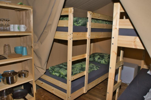 Innenansicht eines Safarizelts mit Etagenbetten, Küchenregal und grüner Bettwäsche im Camping Aller-Leine-Tal.
