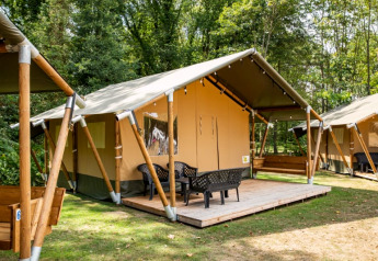Tienda safari con terraza y sillas en un camping boscoso, ideal para glamping y disfrutar la naturaleza.