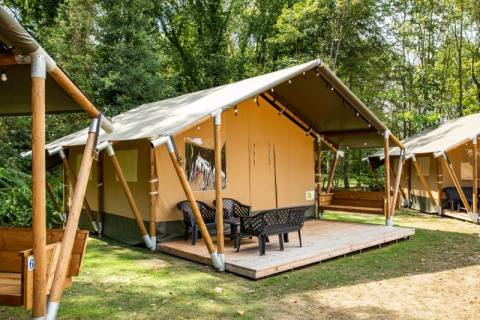 Tienda safari con terraza y sillas en un camping boscoso, ideal para glamping y disfrutar la naturaleza.