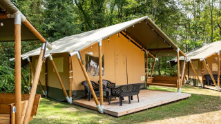 Safari tent met stoelen op houten terras, gelegen op een groene camping, ideaal voor glamping.