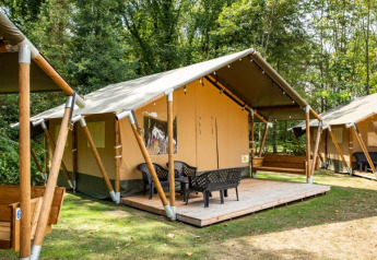 Tienda safari con terraza y sillas en un camping boscoso, ideal para glamping y disfrutar la naturaleza.