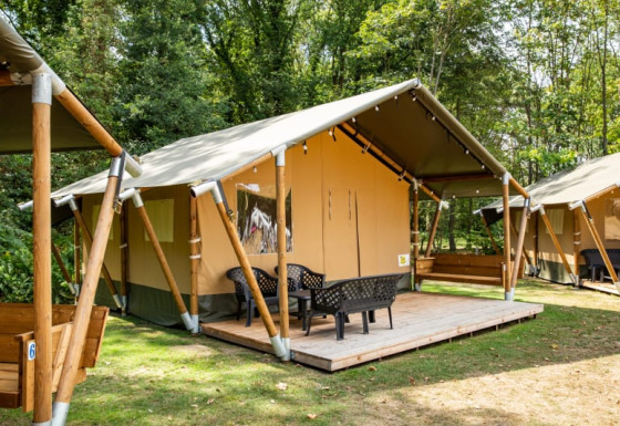 Tienda safari con terraza y sillas en un camping boscoso, ideal para glamping y disfrutar la naturaleza.