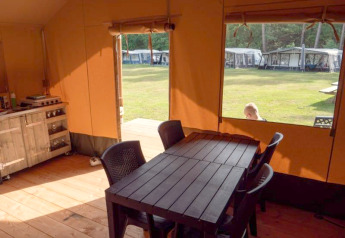 Interior view of safari tent with dining table at Recreatiepark de Wrange, Netherlands, looks outside to grass.
