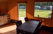 Interior view of safari tent with dining table at Recreatiepark de Wrange, Netherlands, looks outside to grass.
