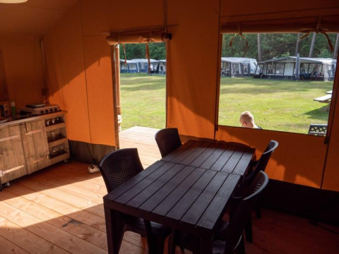 Interior view of safari tent with dining table at Recreatiepark de Wrange, Netherlands, looks outside to grass.
