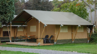 Photo of a large safari tent at a campsite with a covered deck, outdoor table, chairs and green lawn.