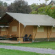 Billede af en stor safari-telt på en campingplads med veranda, borde, stole og grønne omgivelser.