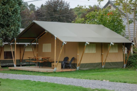 Foto eines großen Safari-Zeltes auf einem Campingplatz mit Veranda, Tischen, Stühlen und viel Grün.