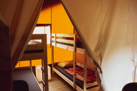 Vista interior de una tienda safari con literas de madera, ropa de cama cálida y paredes de lona.