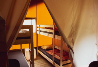 Vista interior de una tienda safari con literas de madera, ropa de cama cálida y paredes de lona.