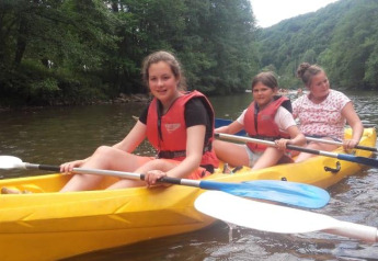 Tres niñas remando en un kayak amarillo en el río cerca de Safari tent en Camping Village Sy, Bélgica.
