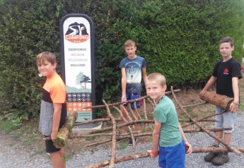 Quattro bambini trasportano rami davanti a un cartello di benvenuto alla Safari tent del Camping Village Sy in Belgio.