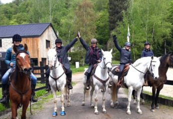 Fem personer på heste foran Safari tent på Camping Village Sy i Belgien, omgivet af grønne træer.