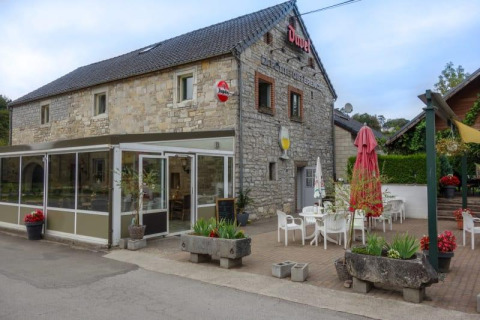 Edificio in pietra con area caffè all'aperto al Camping Village Sy, Belgio, con tavoli e sedie bianche.