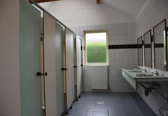 Baño público con cabinas, lavabos y espejos dentro de una tienda Safari en Camping Village Sy, Bélgica.