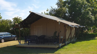 Tenda safari al Camping Eefting nei Paesi Bassi con veranda, sedie esterne e alberi verdi dietro.