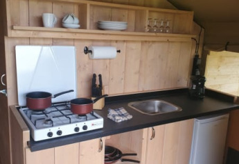 Pequeña cocina de madera en tienda safari en Moulin du Pommier Glamping & Camping en Francia con estufa.