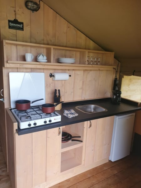 Small wooden kitchen inside a safari tent at Moulin du Pommier Glamping & Camping in France with a stove.