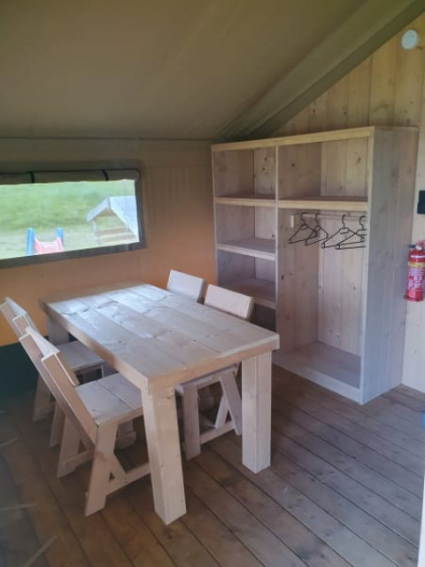 Vista interior de una tienda safari con mobiliario de madera rústica y armario en Moulin du Pommier Glamping, Francia.