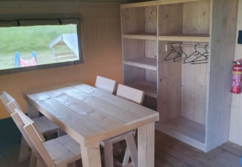 Vista interior de una tienda safari con mobiliario de madera rústica y armario en Moulin du Pommier Glamping, Francia.