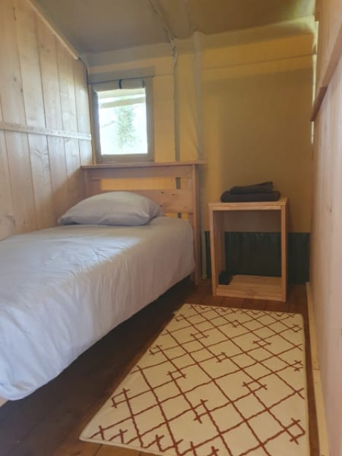 Intérieur d'une tente safari au Moulin du Pommier Glamping & Camping en France, avec lit simple et mobilier en bois.