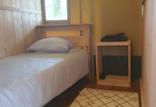 Interior de una tienda safari en Moulin du Pommier Glamping & Camping en Francia, con cama individual y muebles de madera.