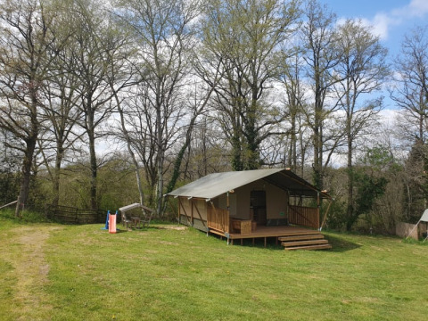 Tente safari au Moulin du Pommier Glamping & Camping en France, entourée d’arbres et de verdure.