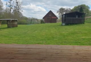 Udsigt fra en safari-teltterrasse ved Moulin du Pommier Glamping & Camping, grøn græsplæne og hytter.