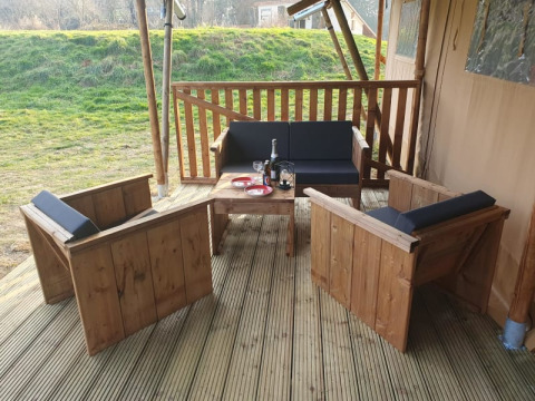 Zona de estar exterior junto a tienda safari en Moulin du Pommier Glamping & Camping, con muebles y vino.