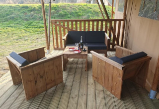 Outdoor wooden seating area at Safari tent at Moulin du Pommier Glamping & Camping, with wine on table.
