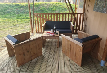 Zona de estar exterior junto a tienda safari en Moulin du Pommier Glamping & Camping, con muebles y vino.